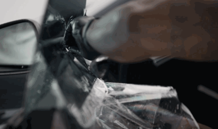 A close-up of a gloved hand peeling old, dark window tinting film from a car side window.