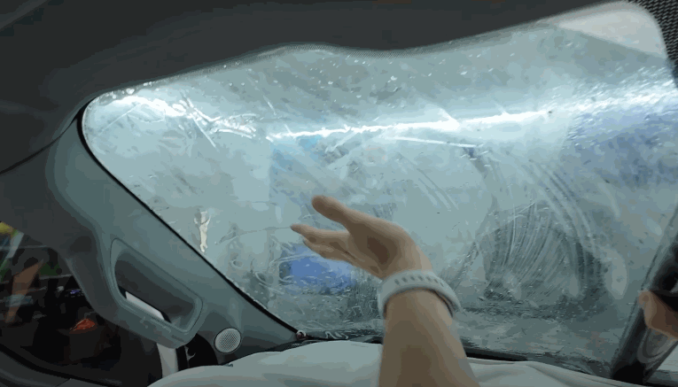 A person smooths out a sheet of window tint film on the inside of a car windshield, using their hand to press it against the glass.