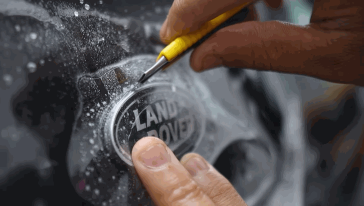 Detailer cutting paint protection film precisely around a Land Rover emblem.