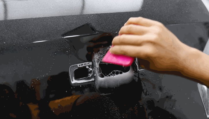 Technician pressing paint protection film into place around a car’s handle area with a pink tool.