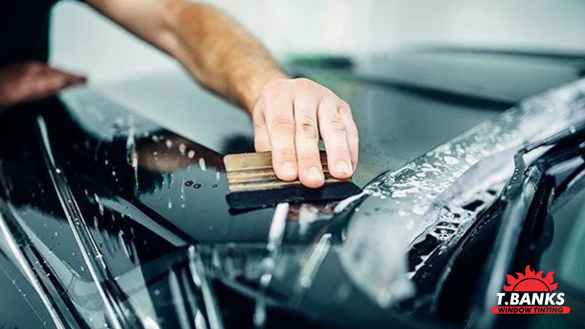 Close-up of installer using a squeegee to apply paint protection film to a glossy black hood.