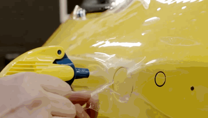 Installer applying paint protection film to the curved surface of a yellow sports car.