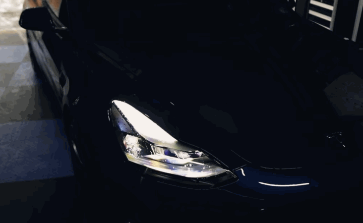 A glossy black Tesla reflects bright overhead lights after a ceramic coating treatment, emphasizing its mirror-like finish.