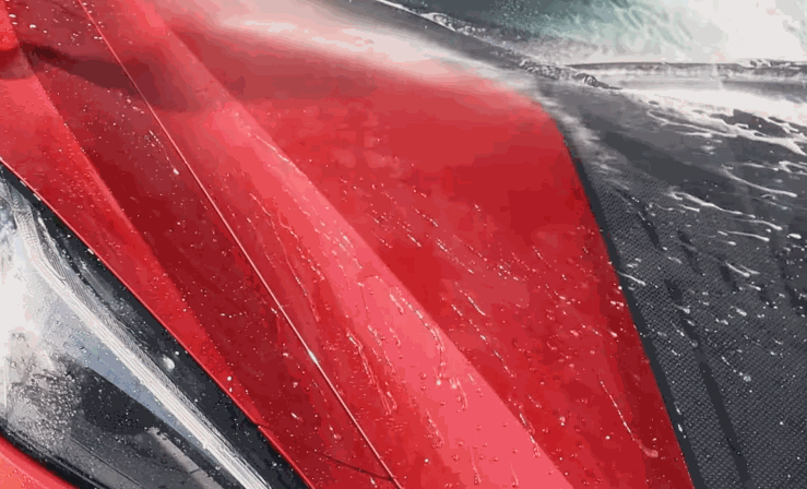 Water is sprayed on a red and black car hood, instantly beading and rolling off the ceramic-coated surface.