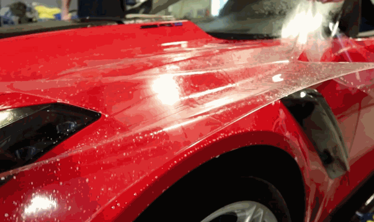 A red Corvette hood being sprayed with water, showing water beading from a ceramic-coated surface.
