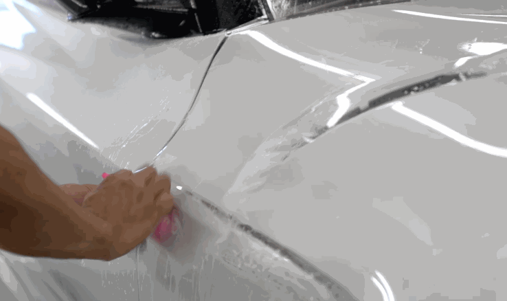 Ceramic coating or PPF being applied to the white body panel of a vehicle using a squeegee tool.