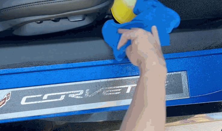 Person applying ceramic coating to the door sill of a blue Corvette using a microfiber cloth and applicator pad.