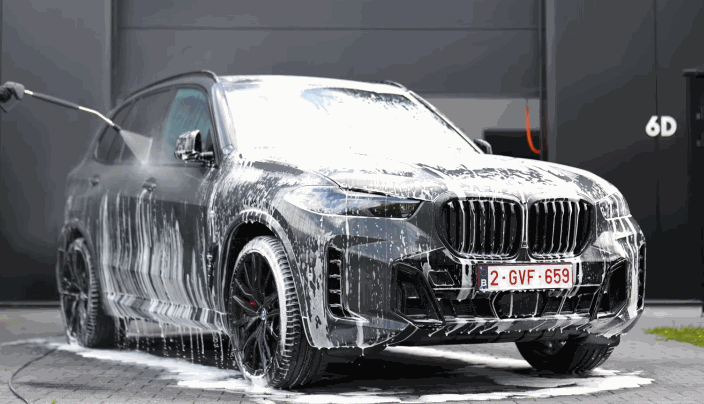 Black BMW SUV being foam-washed as part of the ceramic coating removal prep process.