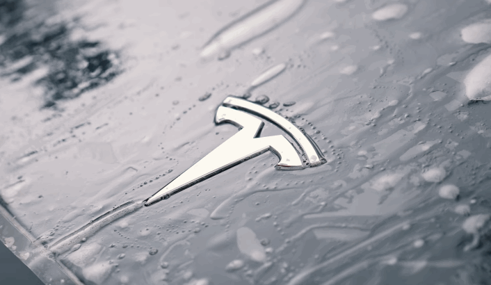 Close-up of a Tesla hood with a wet paint protection film applied over the chrome Tesla emblem.