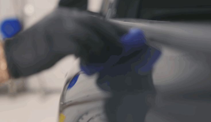 A person buffs a freshly coated car surface with a microfiber towel to remove excess ceramic coating and enhance the finish.