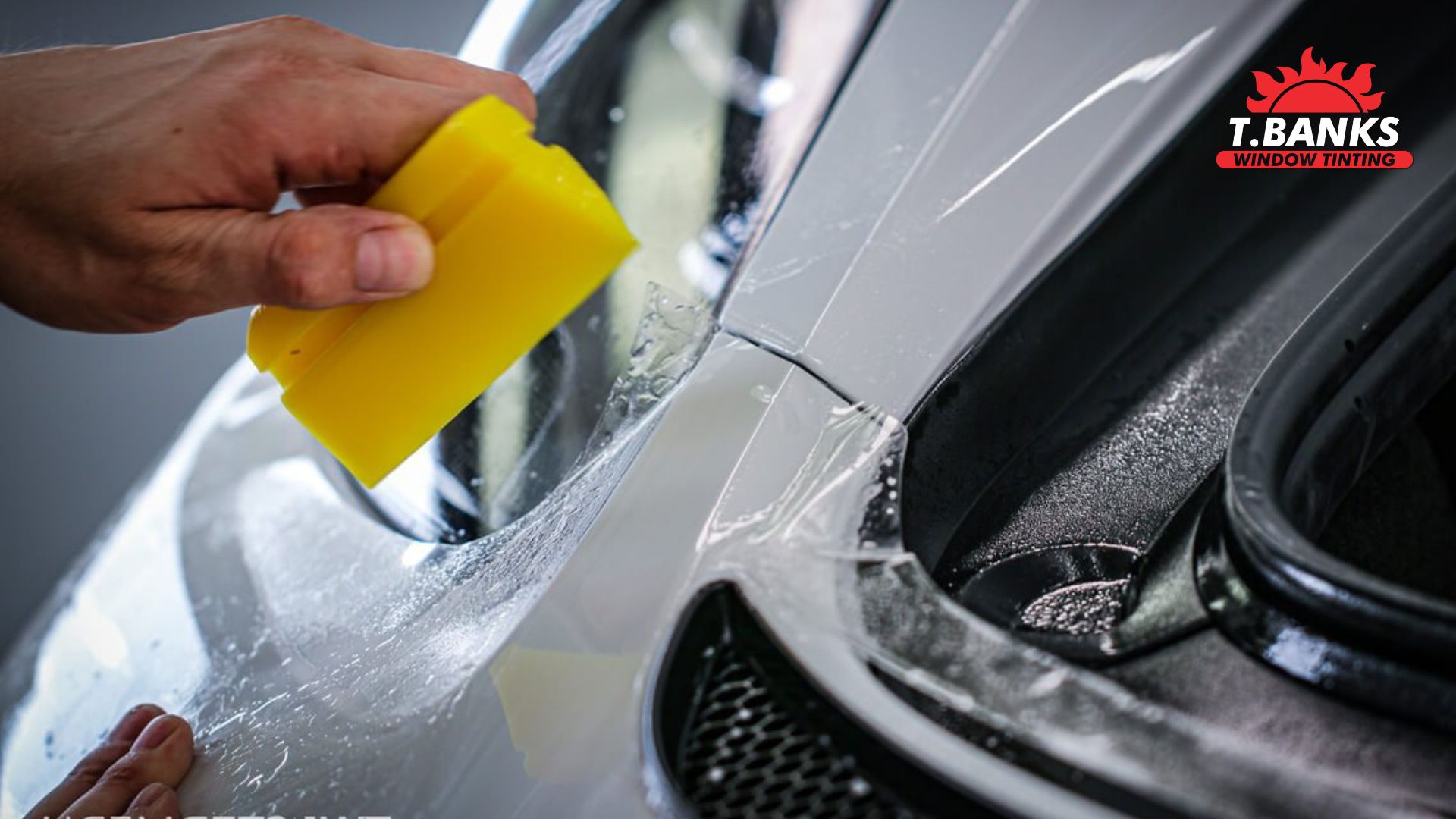Close-up of a yellow squeegee tool pressing down clear paint protection film on the fender of a white sports car during installation.