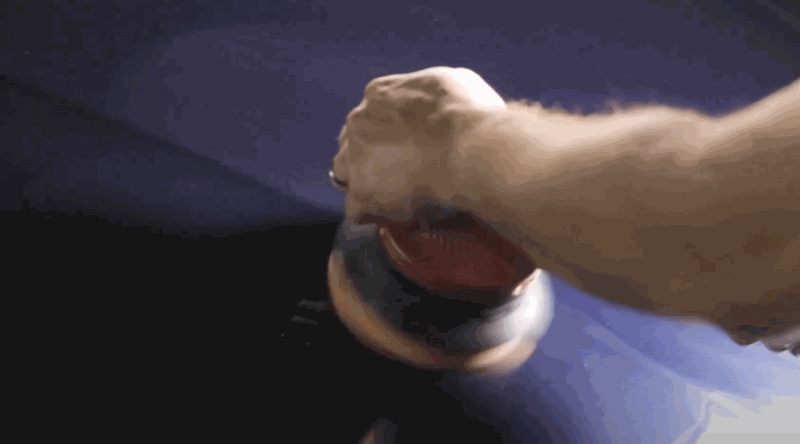A person using a dual-action polisher to buff ceramic coating into a dark-colored car hood.