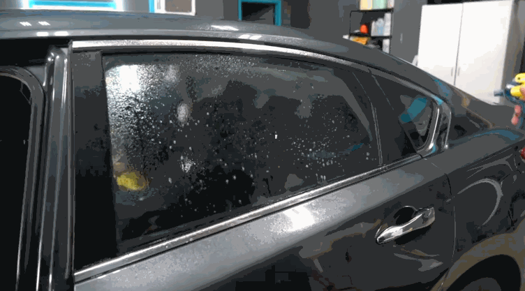 A freshly applied layer of window tint covers a car’s rear door window, with moisture and bubbles still visible as the film settles during installation.