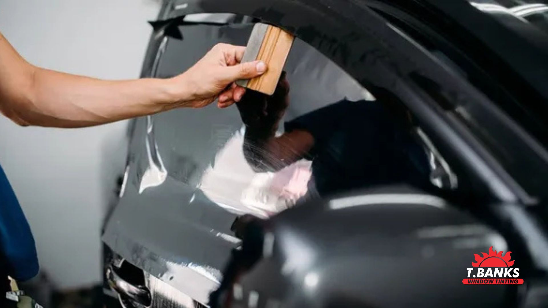 Technician applying window tint film to a car windshield using a small squeegee tool to smooth the material across the glass. The installer’s hand presses the tint firmly against the curved windshield while removing air bubbles during the window tint installation process.