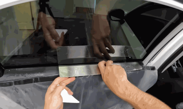 A technician aligns ceramic window tint along the bottom edge of a car side window. The dark film is positioned carefully against the glass for a clean fit.