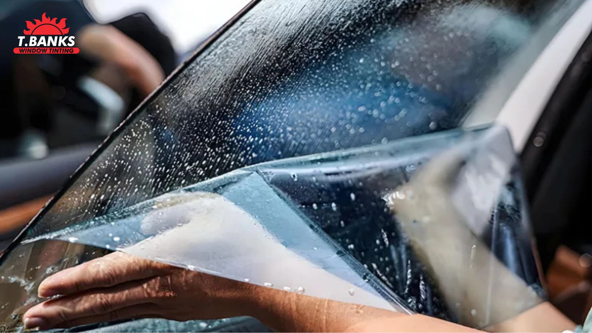 A technician applies ceramic window tint to a wet car window while holding the clear film in place.