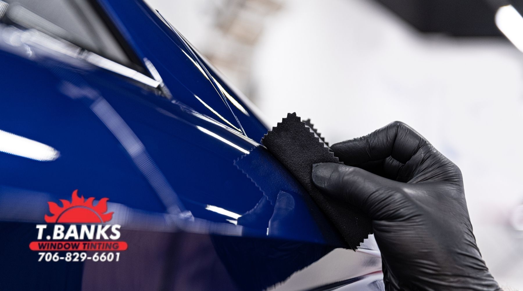 T. Banks Window Tinting technician applying ceramic coating to the glossy blue paint of a vehicle.