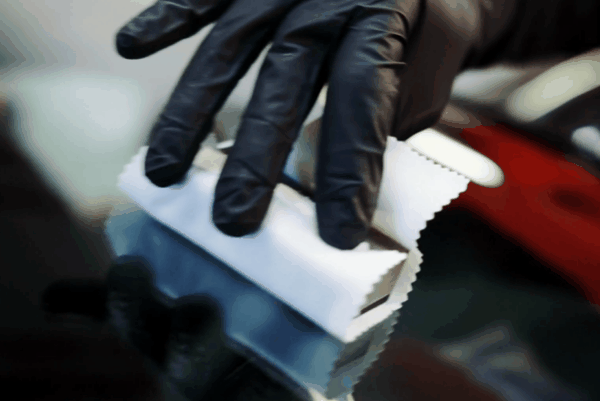 Black-gloved technician applying ceramic coating to a dark vehicle’s paint with a microfiber applicator.
