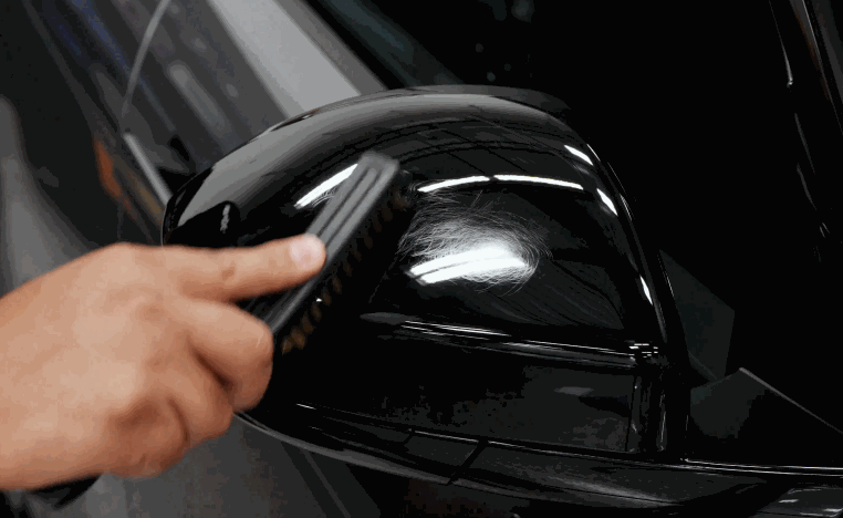 Close-up of a technician working on a black side mirror while preparing it for paint protection film application.