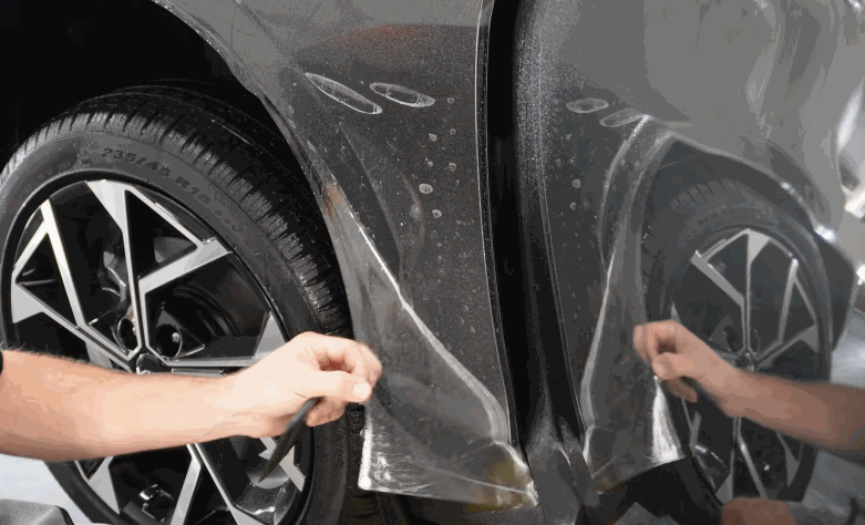 Close-up of paint protection film being positioned along the lower door and wheel arch area of a gray vehicle.