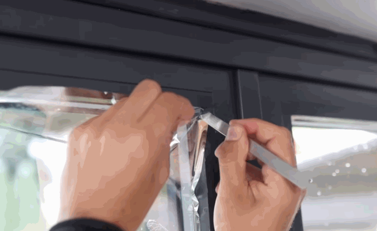 Installer trims home window tint along the edge of a residential glass door with a small blade.