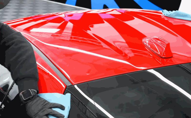 Detailer wipes a glossy red car roof during the ceramic coating process.
